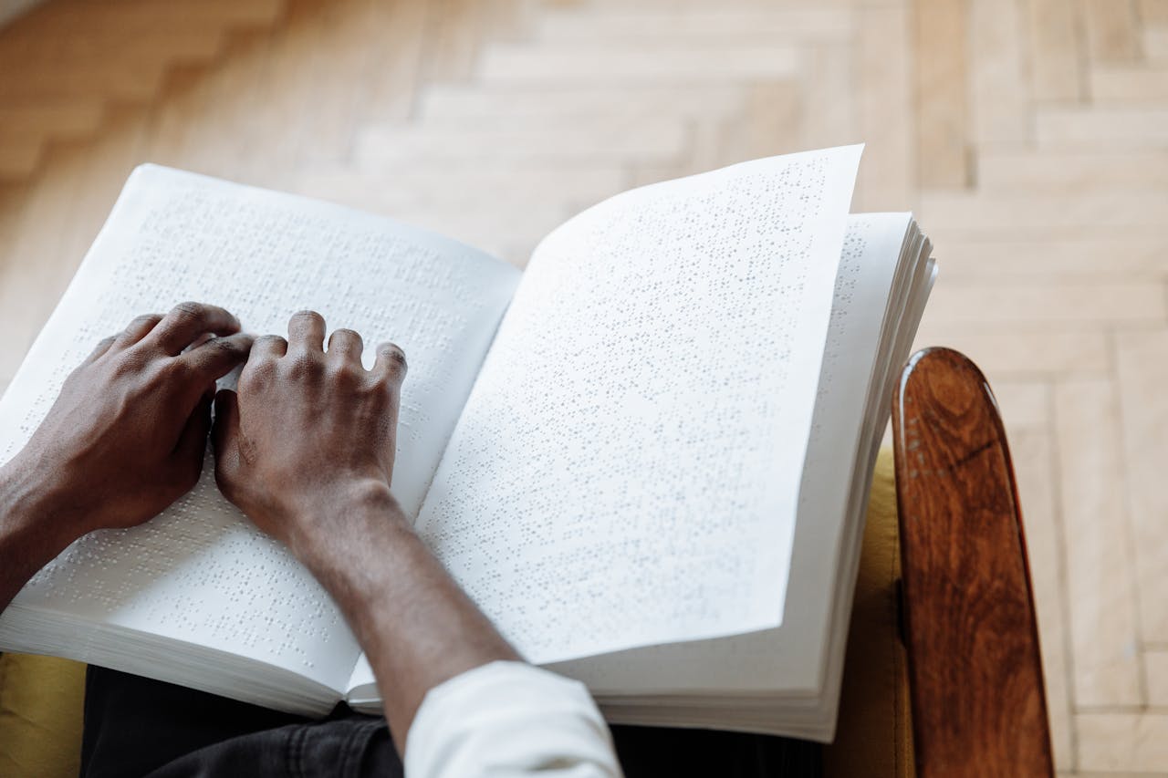 Close-up of hands reading a Braille book, highlighting sensory perception and disability awareness.