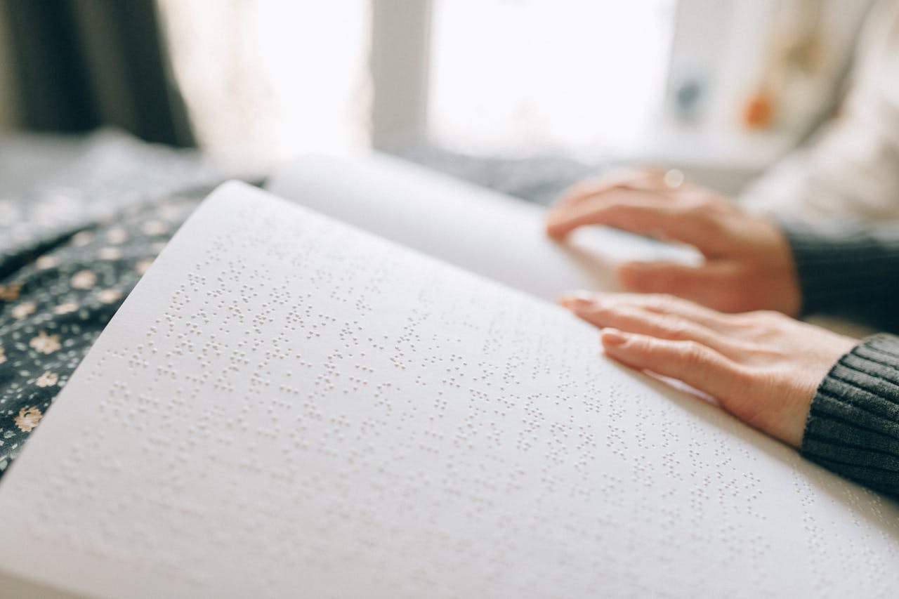 Close-up of hands reading a braille book, emphasizing tactile learning.