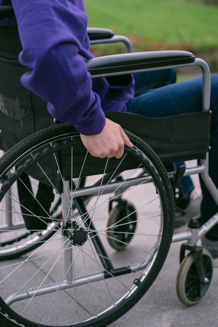 A person in a purple hoodie using a wheelchair on a paved path, highlighting accessibility.