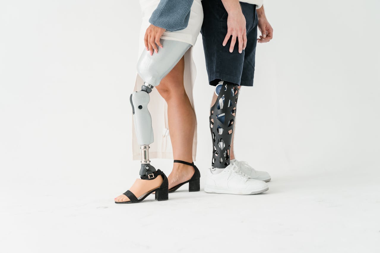 Two adults stand back to back showcasing different prosthetic legs on a white background.